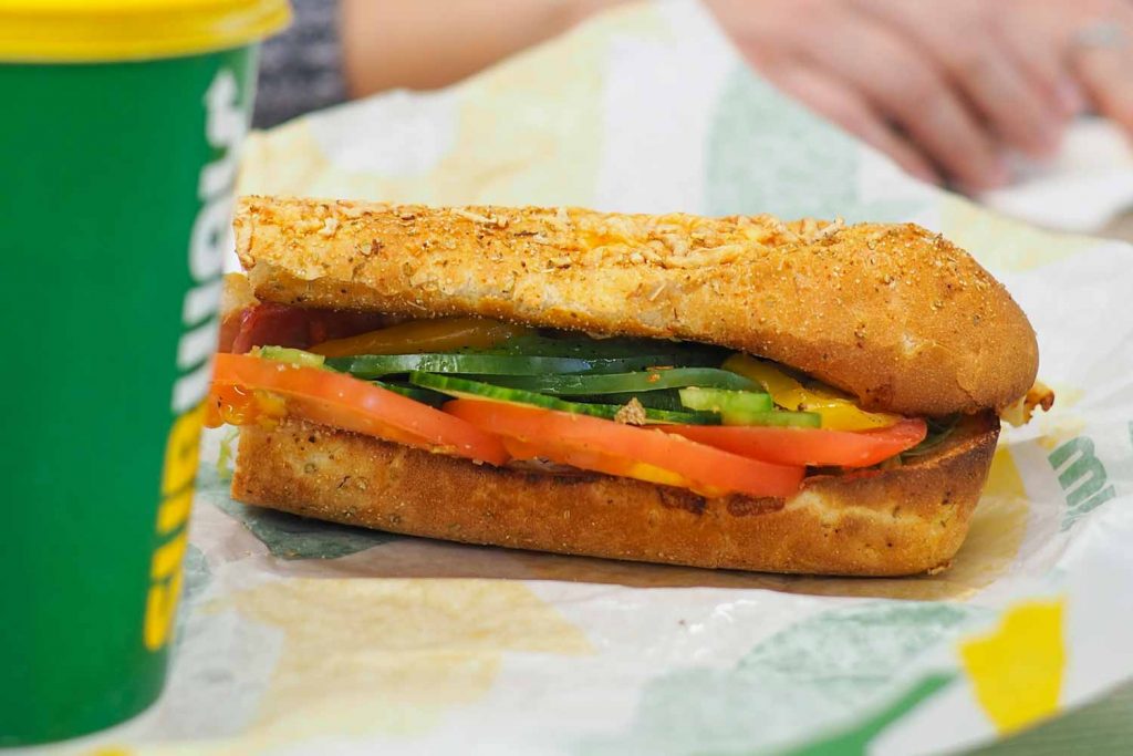 Subway Sandwich with tomatoes and cucumber, laying on wrapper beside a Subway brand cup