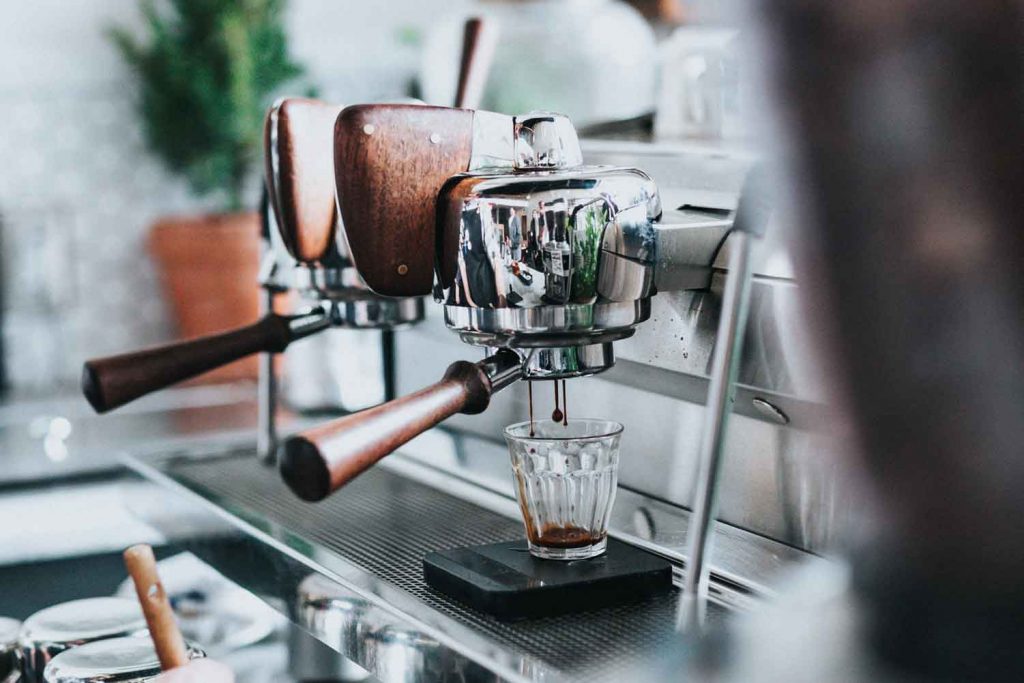 Chrome and wood espresso machine with a shot of espresso being pulled